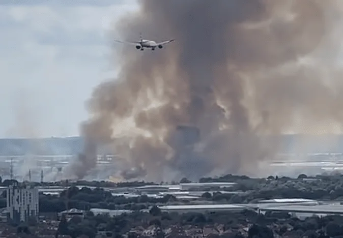 A grass fire involving gas cylinders on Hatton Road in Feltham is being fought by 15 fire engines and approximately 100 firefighters
